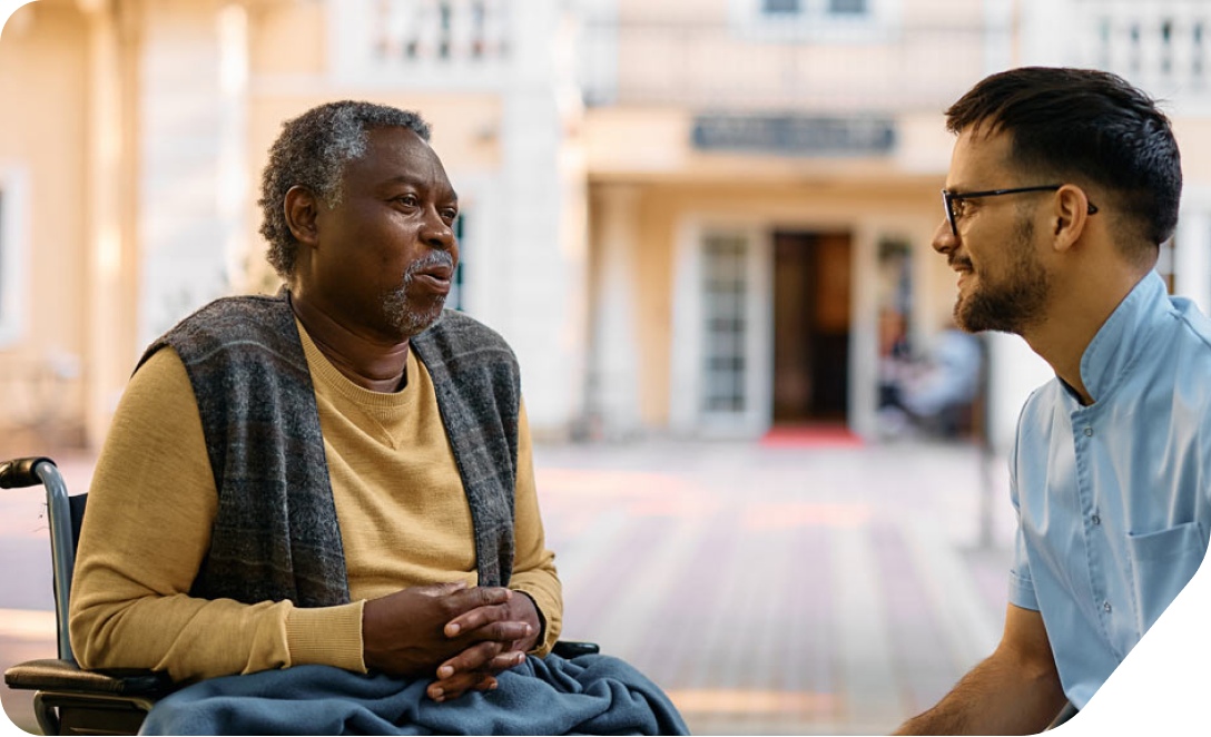 A man in a wheelchair talking to a friend in front of a building