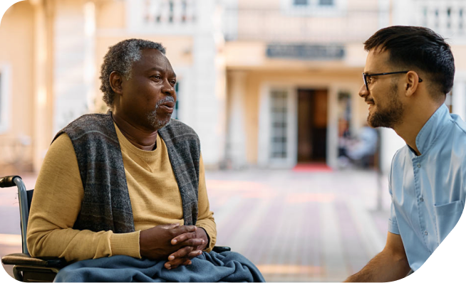 A man in a wheelchair talking to a friend in front of a building